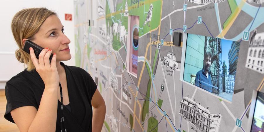 Eine Frau mit Audioguide betrachtet an einem großformatigen Stadtplan einen Film