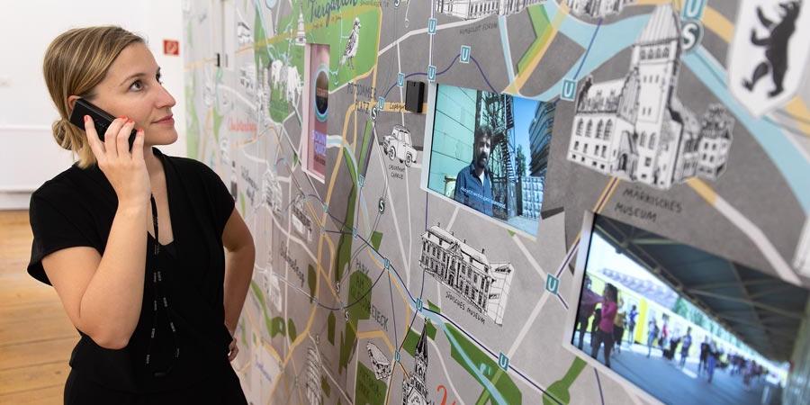 Eine Besucherin der Ausstellung betrachtet mit dem Audioguide am Ohr eine Karte von Berlin