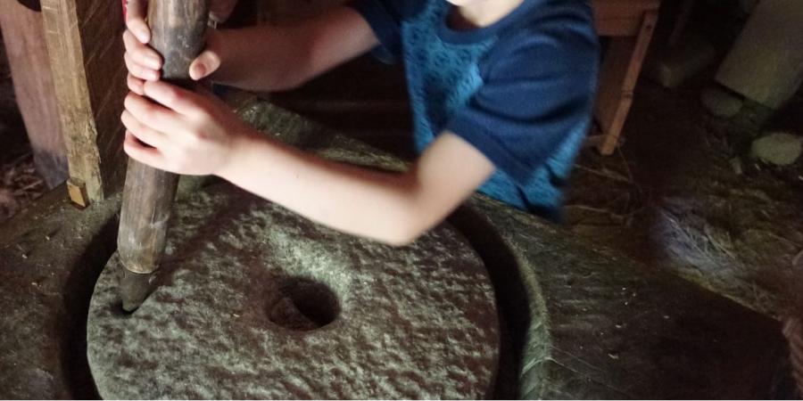 Junge mahlt Korn mittels einer Handmühle