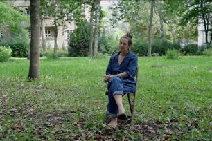 Die interviewte Sibylle Jazra auf einem Stuhl auf einer Wiese unter Bäumen