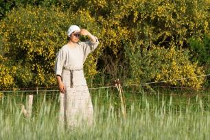 Eine Frau in mittelalterlichem Gewand auf einer Wiese vor Bäumen im Freilichtmuseum