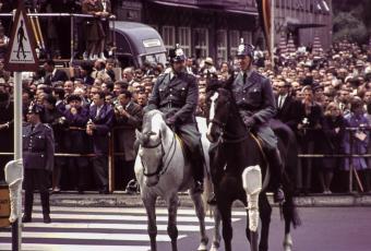 Wartende Kölner und berittene Schutzpolizisten vor einer Tribüne für Medienvertreter am Dom, 23.6.1963