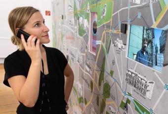 Eine Besucherin mit Audioguide betrachtet an einem großformatigen Stadtplan einen Film