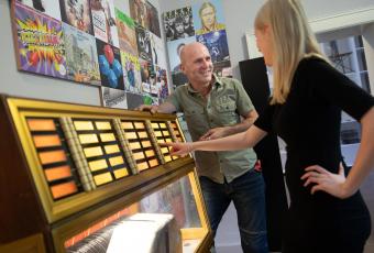 An einer historischen Musikbox erkunden zwei Personen in der Ausstellung den Sound der Stadt.