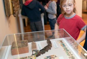 Kinder betrachten eine Vitrine mit Spielzeug aus dem 19. Jahrhundert, darunter eine kleine Dampfeisenbahn, Legespiele und geschnitzte erzgebirgische Holzspielfiguren