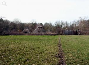 Blick auf ein grünes Feld, im Hintergrund die Häuser des Museumsdorfs Düppel