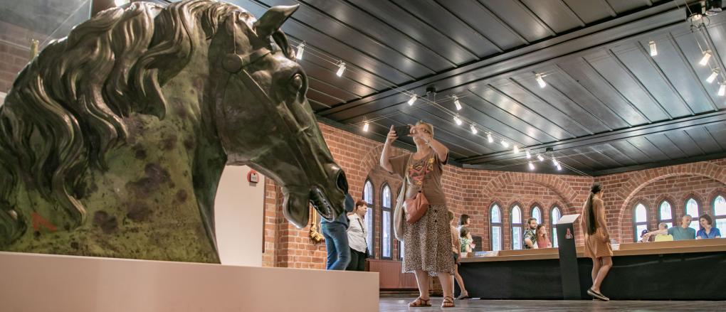 Eine Besucherin fotografiert den bronzenen Pferdekopf in der Ausstellung